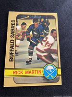 Front side of 1972-73 O-Pee-Chee Rick Martin Buffalo Sabres hockey card in blue and yellow uniform skating on ice