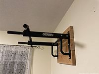 Side view of black metal pull up bar station mounted on natural wood board fixed to wall.