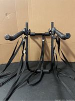 Front view of the black adjustable bicycle rack with foam-padded bars and multiple black adjustable straps hanging below it.