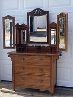 Full frontal image of the antique wooden dresser showing all three mirrors (center tilting and side pivoting mirrors) mounted on top of the dresser body with three drawers and metal handles.
