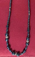 Hematite necklace laid out on a red fabric background showing details of the beads and diamond-like accent beads.