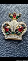 Front view of gold-tone crown brooch/pendant showing red, green, blue, and clear glass gems sparkling in the light.