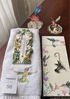 Photo showing hand towel with embroidered hummingbird, decorative thermometer, magnetic hummingbird notepad, spun glass hummingbird figurine, and small stained glass hummingbird sun catcher