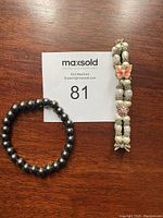 Lot photo of two magnetic bracelets, one featuring two strands with apricot butterflies and pearls, the other a single strand of black onyx colored beads