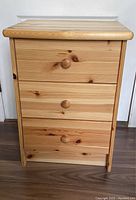 Front view of the pine side table showing three drawers and wooden knob handles.