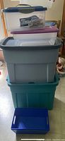 Five plastic storage containers stacked, plus two blue organizing trays in front.
