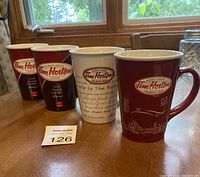 Four Tim Hortons mugs arranged in a row on a wooden table near window