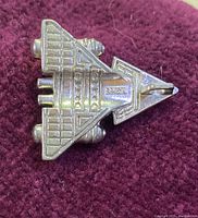 Top view of silver-tone spaceship pendant against dark fabric, showing detailed surface and bail for chain.
