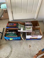Boxes containing an assortment of books, DVDs, and CDs placed on the floor in front of a door.