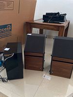 Pair of Bose stereo speakers and Samsung wireless active subwoofer shown with wood table in background