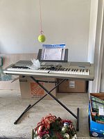 Overview photo shows Casio WK-200 keyboard set on black adjustable stand in a garage setting with tennis ball hanging and boxes visible.