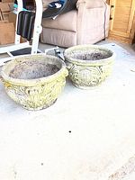 Pair of two large round cement planters with decorative classical relief patterns, showing exterior sides and interior at garage floor location.