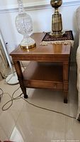 Full view of Drexel wood end table in brown finish with bottom shelf and drawer. Items on top not included.