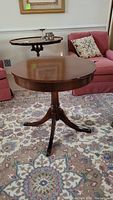 Overall view of round dark wood drum table with pedestal base and four legs on an area rug in a living room setting.