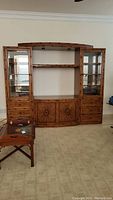 Front view of entire rattan-style entertainment wall unit showing center TV console, glass door sides with shelves and drawers, bottom cabinet doors with sunburst design.