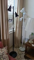 Pair of metal floor lamps side by side, one black with stainless steel trim, one white, each with three lights and cords visible on floor