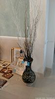 Full view of the dark pottery floor vase with faux branches inside, placed on tile floor near wall and other decor.