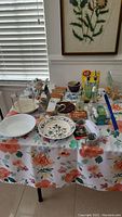 Overview photo of assortment of kitchenware including bowls, teapots, oil and vinegar bottles, coasters, and kitchen gadgets on a floral tablecloth.