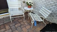 Wide shot of the patio side table with two metal framed chairs with plastic strapping seating and backs, showing overall condition and setup.