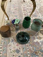 Photo of various ceramic pottery items with diverse colors and shapes, including vases, a bowl, and decorative frog.