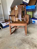 Front view of wooden rocking chair showing vertical slat backrest and wicker seat.