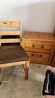 Side view of the wooden chair and two-drawer side table showing finish wear and detailing of handles and cushion.
