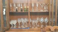 Various wine, martini, and appertif stemware displayed inside a wooden cabinet, showing multiple types and styles including some Roemer goblets with green bases.