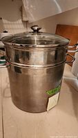 Stainless steel stockpot with glass lid on top placed on counter.