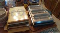 Bella Cucina three-part ceramic buffet server with blue floral pattern stacked beside two stainless steel warming trays on a table with other dishware in background.