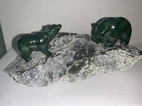Two green Alaskan jade animal figurines on natural stone base seen from a side angle