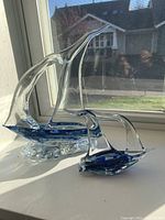 Two hand blown clear glass boats with blue detail sitting on a windowsill, showcasing their size and shape.