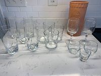 Photo showing various bar glasses arranged on a countertop with a stoneware wine cooler in the background.