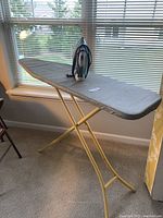 Ironing board set up with iron placed on top by a window.
