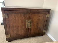Front view of fruitwood console cabinet with brass corner brackets and central brass closure.