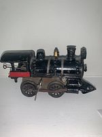 Side view of black cast iron wind-up toy train engine with red rear cab and wind-up key on side, showing detailed rivets and smokestack.