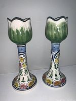 Side view of pair of hand-painted ceramic candlestick holders with floral decorative base and tulip-shaped green tops.