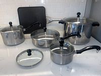 Overall view of all pots with lids and the Calphalon griddle showing condition and included items.