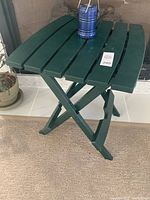 Green folding camp table with plastic slat top and X-frame legs photographed indoors on carpet.