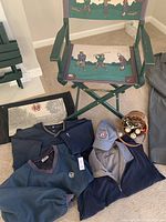Overall view of golf folding directors chair with printed golf player fabric, golf apparel including pullovers and vest, US Open 2010 cap, basket of golf balls, tees, and markers