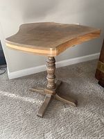 Side view of handcrafted walnut slab table showing wood grain, irregular edge, and carved pedestal base with four flat legs.