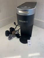 Front view of the Keurig single cup coffee maker with several reusable pods positioned in front of it on a white surface.