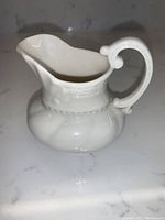 Full side view of Lenox white porcelain creamer pitcher with ornate handle and embossed neck detailing