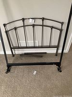 Black metal twin bed headboard with attached frame shown against a wall, featuring spindle vertical rods and horizontal supports.
