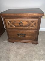 Front view of wooden nightstand showing two drawers with metal pulls and carved X-patterns on top drawer.