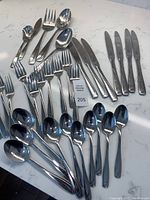 Photo showing the complete spread of flatware on a countertop including teaspoons, butter spreaders, dinner forks, soup spoons, dessert forks, and serving pieces.