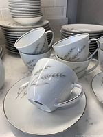 Teacups stacked on saucers showing wheat stalk silver design with silver rim