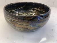 Side angle view of round pottery bowl with dark and light multicolor drip glaze.