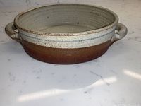 Side view of the round pottery dish showing two handles and gradient glaze from brown to light speckled finish.