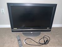 Front view of SONY Bravia TV on swivel stand, remote control, and power cord placed on carpeted floor.