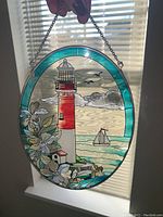 Front view of the stained glass lighthouse hanging with vibrant colors and textured glass showing the ocean, clouds, and flowers.